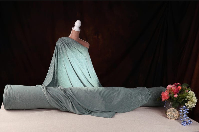 a mannequin wearing a green dress, with a vase of flowers placed next to it on a table.