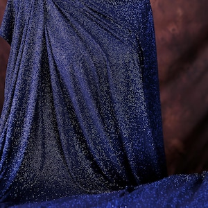 A mannequin wearing a navy blue, sparkly fabric draped over its body.