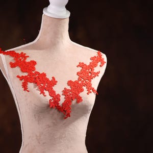 Puede incluir: Borde de encaje rojo con diseño floral. El encaje es delicado e intrincado, y sería perfecto para agregar un toque de elegancia a cualquier prenda.