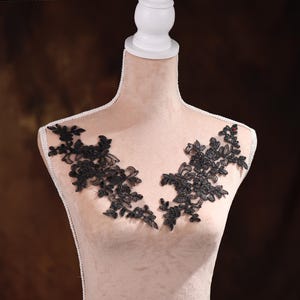 Könnte beinhalten: Eine schwarze Spitzenapplikation mit floralem Muster, auf einer weißen Schaufensterpuppe ausgestellt.