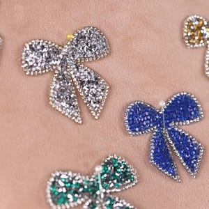 a close-up view of several decorative bow-shaped embellishments, including rhinestones and gemstones, arranged on a light-colored surface.
