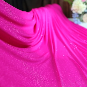 A close-up view of a vibrant pink fabric with a sparkly texture, creating a visually striking contrast against the blurred background.