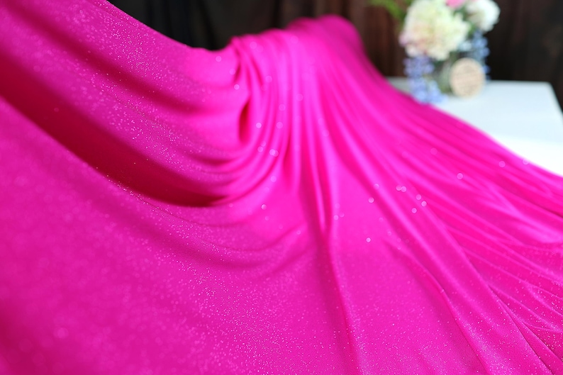 A close-up view of a vibrant pink fabric with a sparkly texture, creating a visually striking contrast against the blurred background.