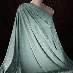 A mannequin wearing a flowing, mint green fabric draped over its body, creating a draped and flowing silhouette.
