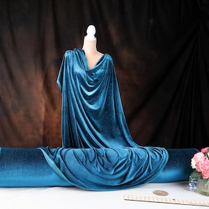 a mannequin dressed in a blue velvet gown, placed on a table with a vase of pink flowers.