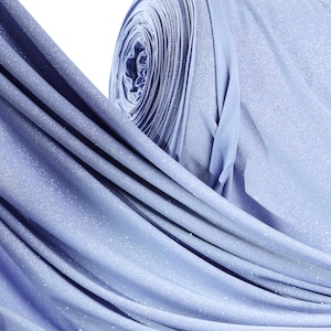 Op de afbeelding: Een rol lichtblauwe stof met een subtiel glittereffect. De stof is gedrapeerd en onthult plooien en texturen. Het materiaal lijkt zacht en vloeiend, met een lichte glans. De achtergrond is wit.