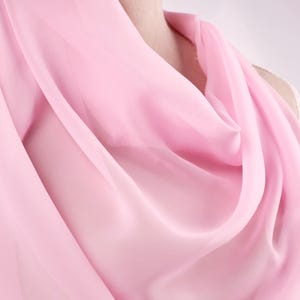 A close-up view of a soft, flowing pink fabric draped over a person's body.