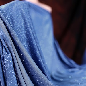 A close-up view of a blue fabric with sparkles, held in a hand.