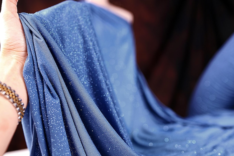 A close-up view of a blue fabric with sparkles, held in a hand.