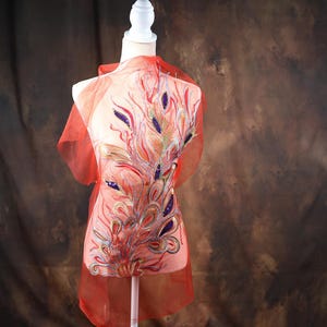 Puede incluir: Una tela roja transparente con un gran diseño de pavo real bordado en tonos dorados, morados y blancos.