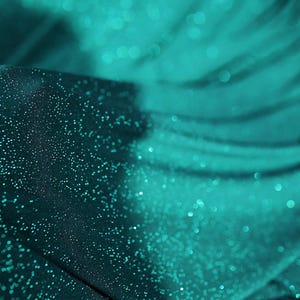 A close-up view of a fabric with a shimmering, glittery texture in shades of blue and green.