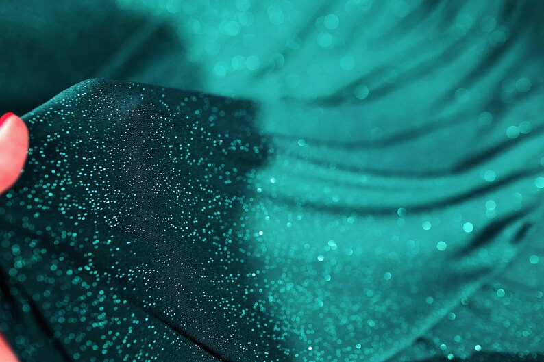 A close-up view of a fabric with a shimmering, glittery texture in shades of blue and green.
