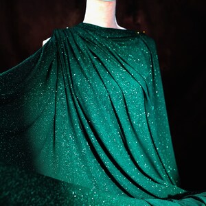 A mannequin wearing a shimmering green dress with a flowing, draped design.