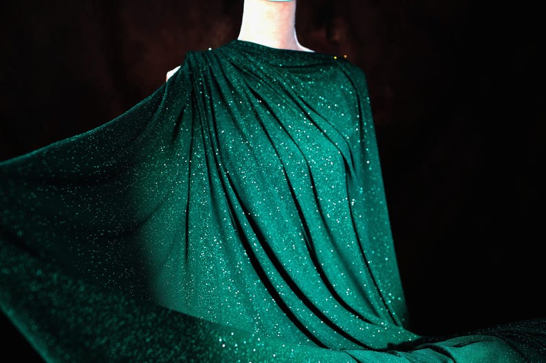 A mannequin wearing a shimmering green dress with a flowing, draped design.