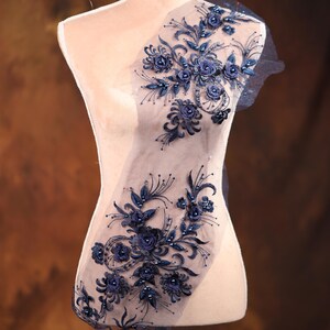 May include: A navy blue floral lace applique with 3D flowers and beads. The lace is on a sheer mesh fabric.