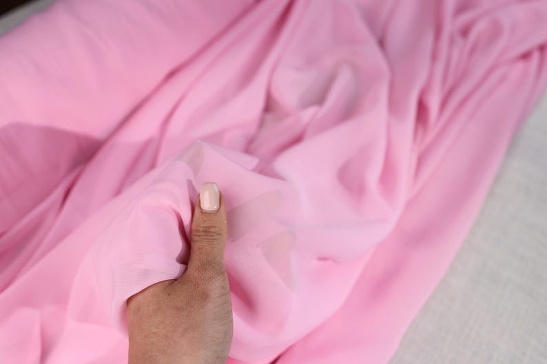 A hand is holding a pink fabric, possibly silk, with a close-up view of the fabric's texture and color.