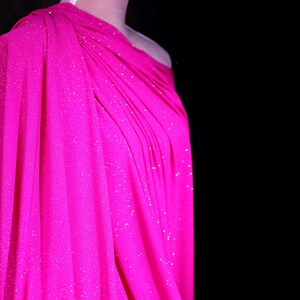 A mannequin wearing a bright pink, sparkly dress against a dark background.