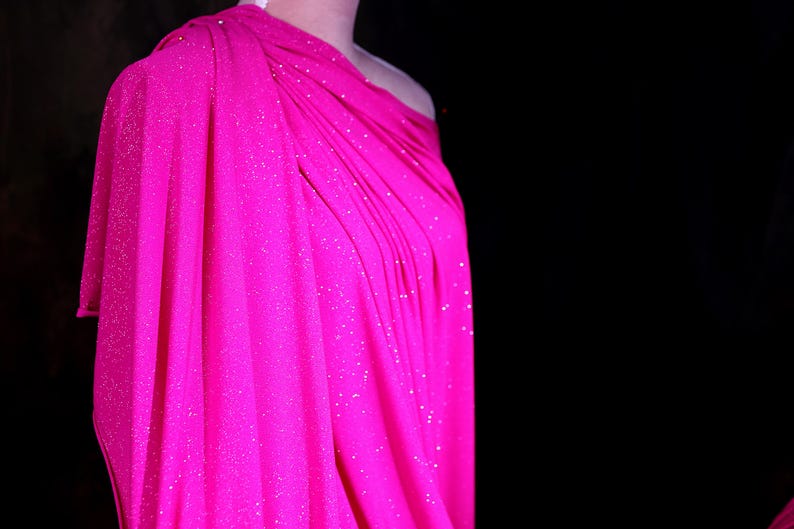 A mannequin wearing a bright pink, sparkly dress against a dark background.