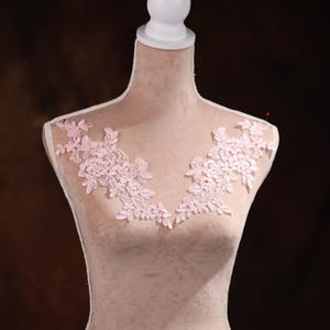 Könnte beinhalten: Eine rosa Spitzenapplikation mit Blumenmuster. Die Applikation befindet sich auf einer weißen Mannequin-Büste.