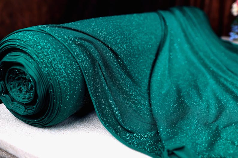 A roll of teal-colored fabric with a glittery texture, lying on a white surface.