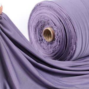 A hand is holding a roll of purple fabric, which appears to be a spool of thread.
