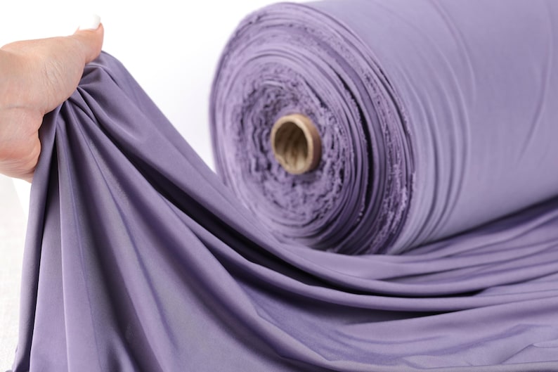 A hand is holding a roll of purple fabric, which appears to be a spool of thread.