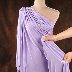 A mannequin wearing a lavender one-shoulder dress is being adjusted by a person's hand.