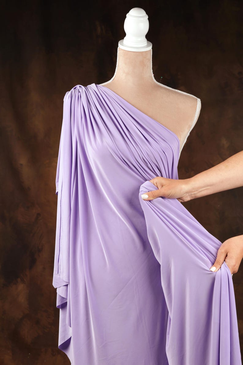 A mannequin wearing a lavender one-shoulder dress is being adjusted by a person's hand.