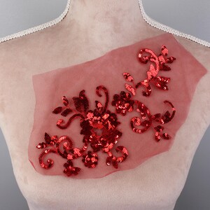 Puede incluir: Aplique floral de lentejuelas rojas sobre una tela roja transparente. El aplique es un diseño delicado con detalles intrincados.