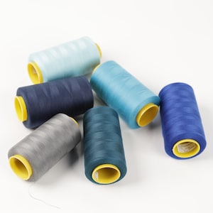 May include: A collection of spools of thread in various shades of blue and gray. The spools have yellow cores and are arranged on a white surface. The threads appear to be tightly wound, and the colors range from light blue to dark navy.