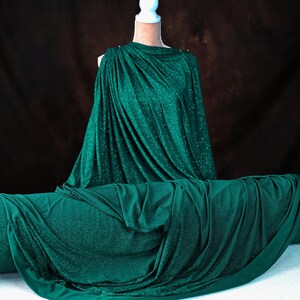 A mannequin wearing a shimmering green dress stands against a dark background.