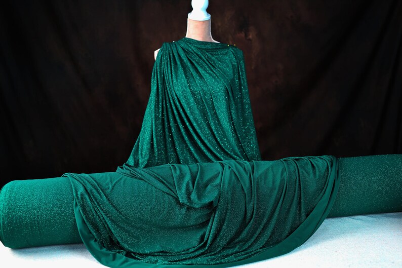 A mannequin wearing a shimmering green dress stands against a dark background.