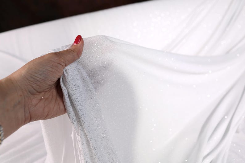 A hand holding a white fabric with a sparkly texture, with the hand appearing slightly wrinkled.