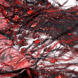 May include: Close-up of a black and red fabric with intricate detailing. The fabric features red sequins and beads, creating a textured, shimmering effect. The design includes flowing lines and floral-like patterns, suitable for apparel or decorative projects.