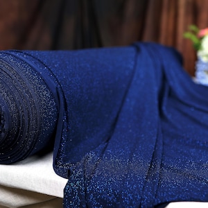 A close-up view of a blue fabric with a glittery texture, resting on a white surface.