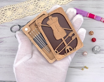 Op de afbeelding: Een houten naaidoos met een uitgesneden ontwerp van een paspop en een veiligheidsspeld. De doos heeft een vak voor naalden en een magnetische sluiting.