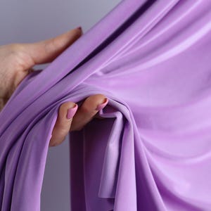 A hand holding a purple fabric, with the fabric partially draped over the hand.