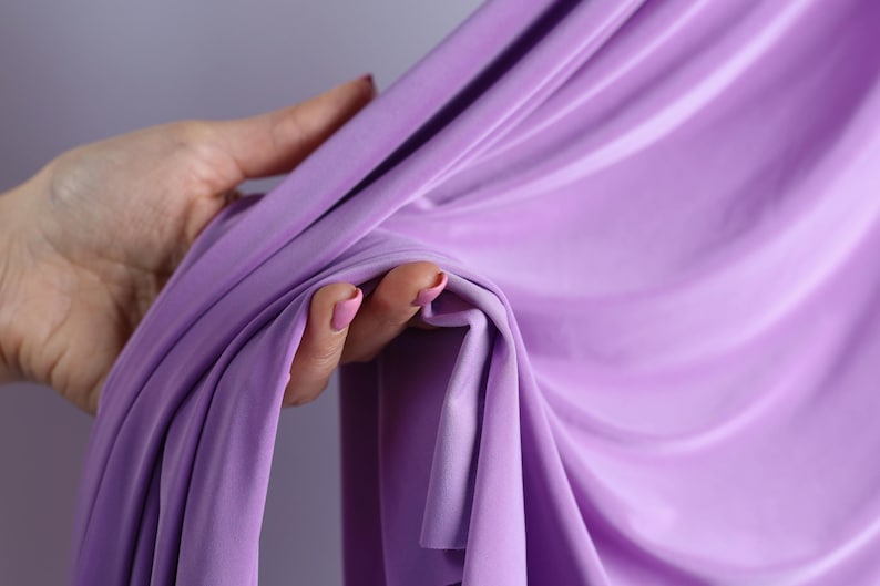 A hand holding a purple fabric, with the fabric partially draped over the hand.
