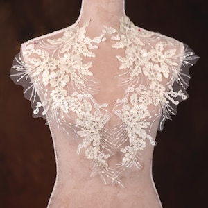May include: A delicate ivory lace applique with floral designs and beaded accents. The lace is perfect for adding a touch of elegance to wedding dresses, bridal accessories, or other special occasion garments.