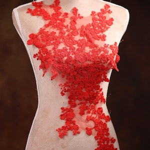 Puede incluir: Aplique de encaje rojo con diseño floral, fijado a un maniquí blanco.