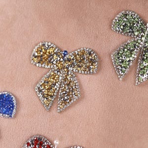 a close-up view of several ornate, sparkling, and colorful jewelry pieces, including a large, eye-catching bow-shaped piece in the center.