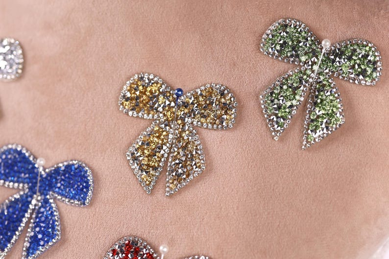 a close-up view of several ornate, sparkling, and colorful jewelry pieces, including a large, eye-catching bow-shaped piece in the center.