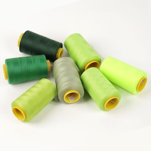 May include: A collection of spools of thread in various shades of green, from deep forest to bright neon. Each spool is cylindrical with a yellow core, perfect for sewing and crafting projects.