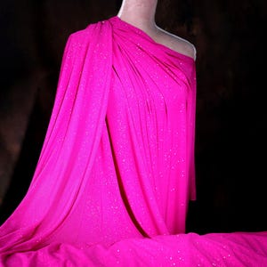 A mannequin wearing a bright pink, sparkly dress stands against a dark background.
