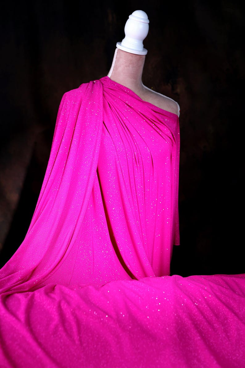 A mannequin wearing a bright pink, sparkly dress stands against a dark background.