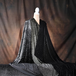 A mannequin wearing a black velvet cape with a shimmering silver and black pattern, set against a brown background.