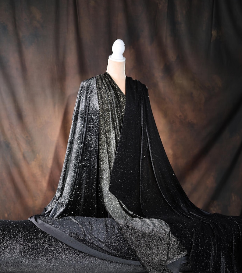 A mannequin wearing a black velvet cape with a shimmering silver and black pattern, set against a brown background.