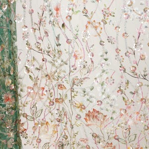 a close-up view of a fabric with a floral pattern, including various shades of green, pink, and white flowers and leaves. The fabric appears to be made of a sheer material, giving it a delicate and airy appearance. The pattern is intricate and detailed, showcasing the craftsmanship involved in creating the fabric.