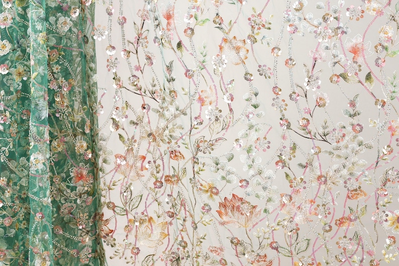 a close-up view of a fabric with a floral pattern, including various shades of green, pink, and white flowers and leaves. The fabric appears to be made of a sheer material, giving it a delicate and airy appearance. The pattern is intricate and detailed, showcasing the craftsmanship involved in creating the fabric.