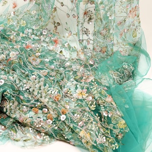 a close-up view of a fabric with a floral pattern, including various shades of green, pink, and white flowers. The fabric appears to be made of sheer material, giving it a delicate and airy appearance.